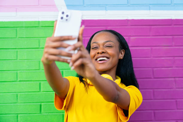 istock Smiling African Woman Capturing Selfie Against Multicolored Wall 2002825163