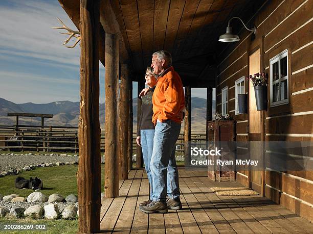 Senior Man And Woman Standing On Porch Embracing Side View Stock Photo - Download Image Now