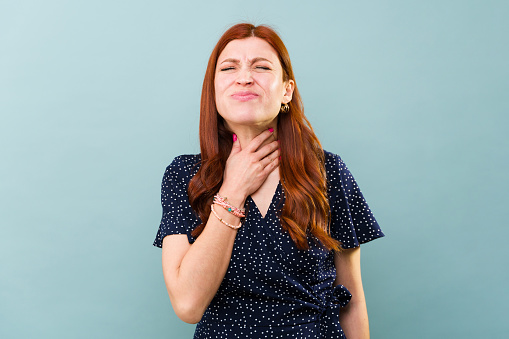 Sick redhead caucasian woman in pain suffering from a sore throat because of a cold or flu