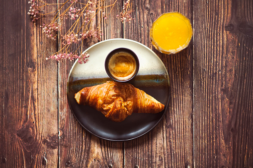 French breakfast with a croissant, orange juice and a coffee. The wooden tabel is decorated with dried pink baby’s breath.