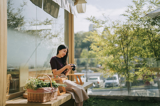 Asian Chinese woman holding camera sitting at terrace in Japanese style exterior design restaurant with Japaneses coffee table set on tatami cushion