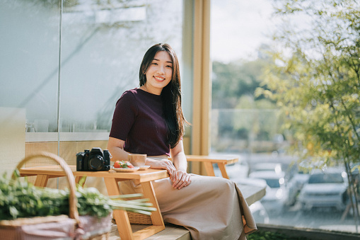 Asian Chinese woman looking at camera smiling sitting at terrace in Japanese style exterior design restaurant with  Japaneses wagashi table set on tatami cushion