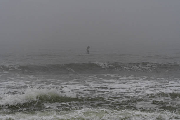 Belmar, New Jersey, USA - Mist Fog and Breaking waves with a silhouetted Stand Up Paddle Boarder in the background