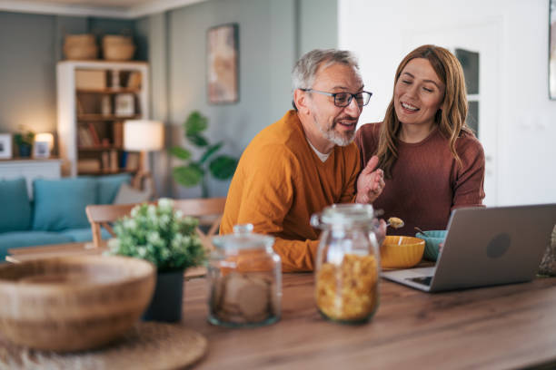 istock Mature couple has breakfast together at home. They enjoy and laugh while talking on a video call. 2002996318