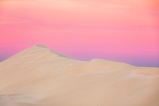 Dry arid desert landscape scene with white sand dunes against a dramatic pink sky. Photographed in Western Australia.