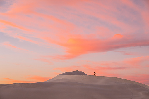 Young backpacker hiking through arid desert landscape scene with white sand dunes against a golden sky. Photographed in Western Australia.