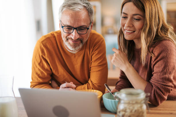 istock Mature couple has breakfast together at home. They enjoy and laugh while talking on a video call. 2003023588