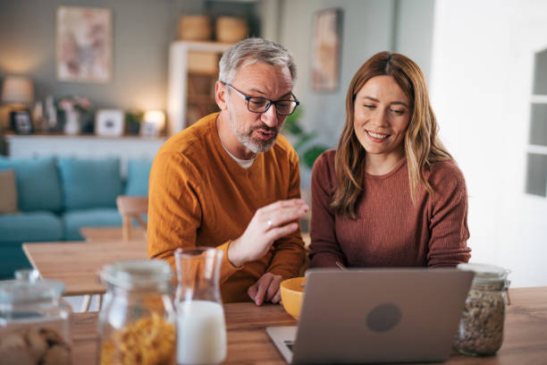 istock Mature couple has breakfast together at home. They enjoy and laugh while talking on a video call. 2003023601