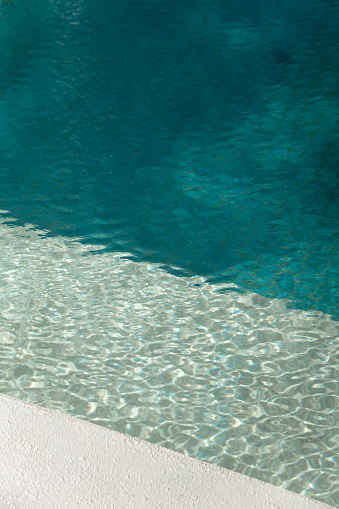 Swimming Pool edge with turquoise tiles and sunlight on water surface