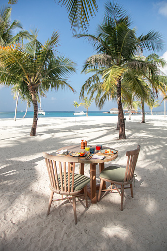 Maldives outdoor breakfast table under tropical palm tree garden with lagoon sea view