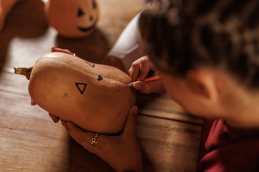 Cut out shot of unrecognizable mother and daughter drawing a Jack o' Lantern on a pumpkin as a Halloween craft decoration.
