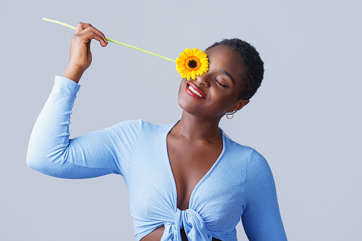 Portrait of a authentic happy young woman holding orange Gerbera daisy covering her eye with eyes closed. Naturally beauty concept.