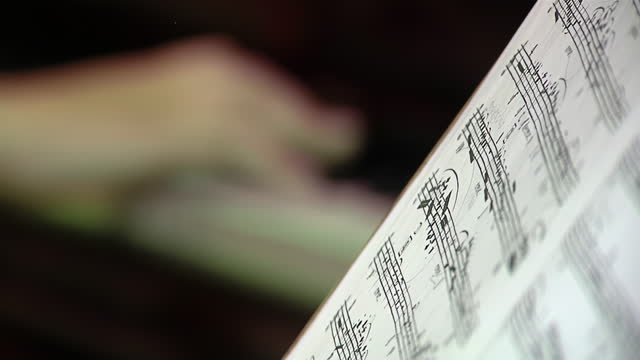 Music Stand and Score and A Pianist Playing A Piano in the Background. Close Up.