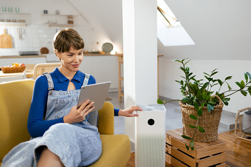 Portrait of a young woman adjusting her home air purifier using a tablet.