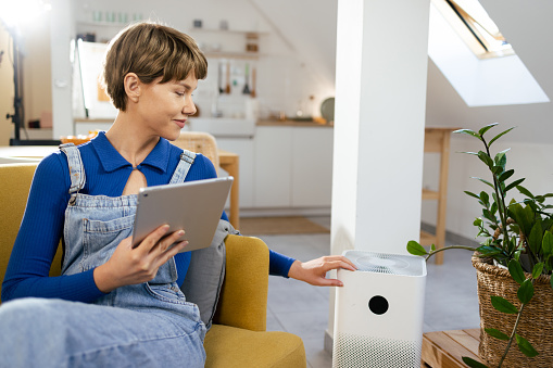 Portrait of a young woman adjusting her home air purifier using a tablet.