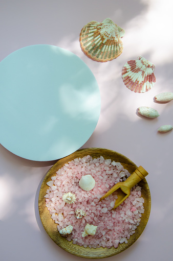 Round white flatlay mockup with spots of light and shadow , white and pink seashells and pink sea salt in a wooden plate with a wooden spoon - spa table
