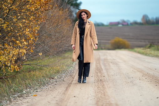 Young beautiful brunette woman in coat and hat on the countryside road