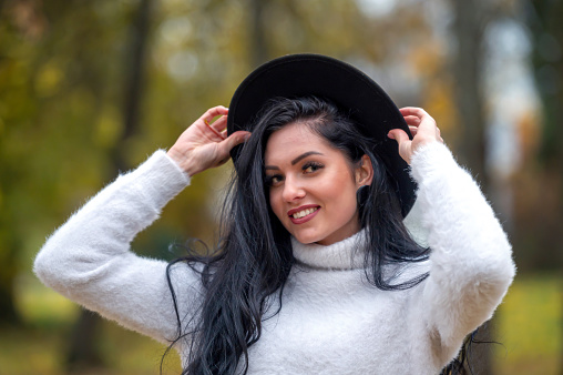 Beautiful young brunette woman in a white sweater and black hat in autumn park