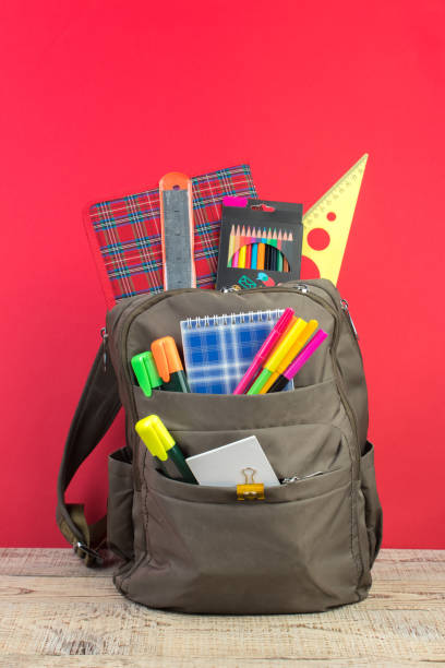 Backpack with different colorful stationery on table. Bright Red background. Back to school
