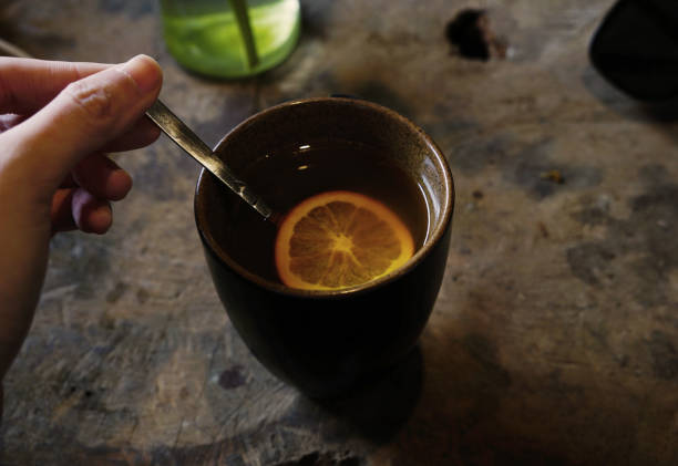 istock Hand holding a spoon stirring a cup of ginger tea with orange slice 2003265906