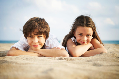 Boy and girl (8-10) lying on beach, smiling, close-up, portrait
