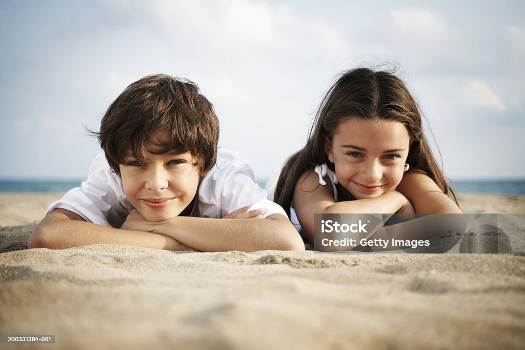 Boy and girl (8-10) lying on beach, smiling, close-up, portrait  Child Stock Photo