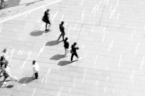 Black and white blurred photo of people walking in city, elevated view, background with copy space, full frame horizontal composition