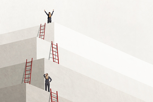 A businesswoman looks up at a woman who has reached the top as she stands next to one of a series of ladders that she has climbed to reach her goal.