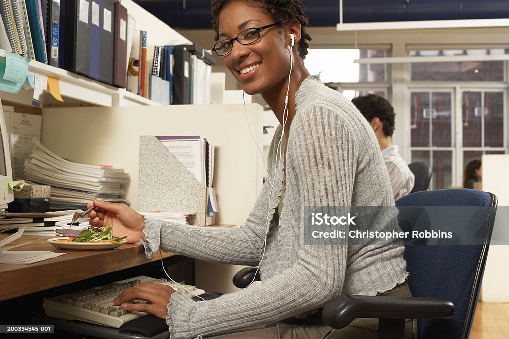 Mujer comiendo en escritorio de oficina, sonriendo, retrato - Foto de stock de Auriculares - Equipo de música libre de derechos