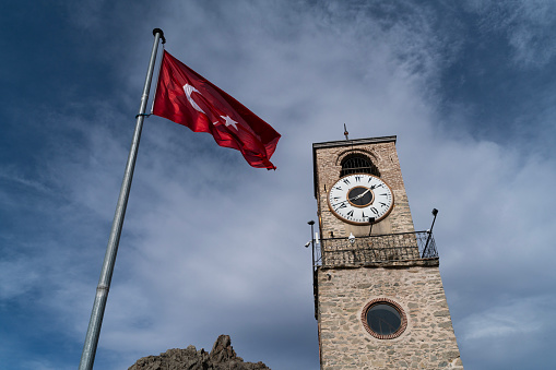 Image of the clock tower and the Turkish flag in the Sivrihisar district of Eskişehir province. Photographed from the bottom angle with the sky. the flag is waving. Taken in daylight with a full frame camera.