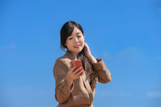 istock Young Asian businesswoman using cell phone on sunny day with blue sky 2003451101