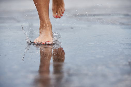 Women's feet make splashes in puddles on the road in the city.