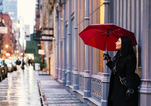 Rear view of a young woman is walking with a red umbrella in the rain, Soho, New York City, USA