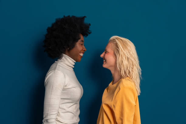 istock Two diverse young women standing together and looking at each other in a studio 2003527389