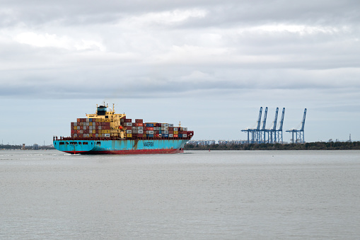 Charleston, SC, USA - February 11, 2024: Maersk container ship Iowa sails into Charleston Harbor, with the ship-to-shore cranes of Hugh K. Leatherman Terminal in the background.