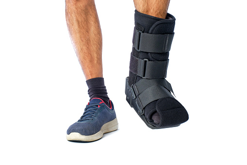 man's legs from the front with an orthopedic boot for breaks and sprains on a white background