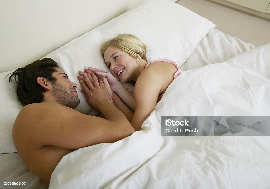 Coppia a letto, con le mani su un cuscino, sorridente - Foto stock royalty-free di 30-34 anni