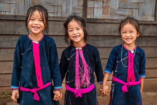Three Laotian little girls, wearing traditional Lantan tribe clothes, sitting on a stairs in a Lantan village in Northern Laos