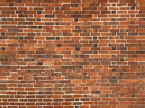 Horizontal closeup photo of an old brick wall on the side of a building with a variety of small and larger orange brown toned bricks with limestone mortar. Uralla, New England high country NSW.