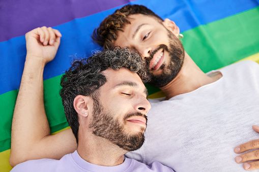 Gay couple enjoying gay pride day lying on top of rainbow flag. Relaxed and smiling attitude. Fighting for LGBT rights