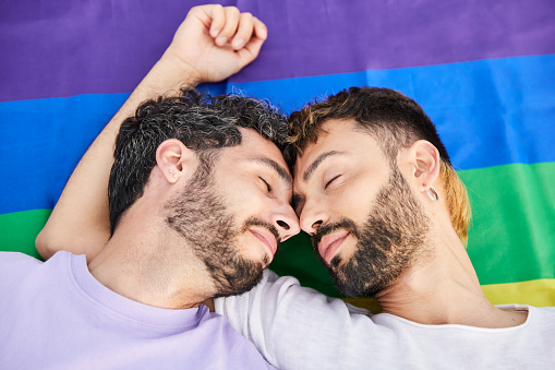 Gay couple enjoying gay pride day lying on top of rainbow flag. Relaxed and smiling attitude. Fighting for LGBT rights