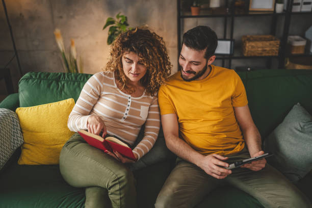 istock man and woman read book and use digital tablet at home on sofa bed 2003602136