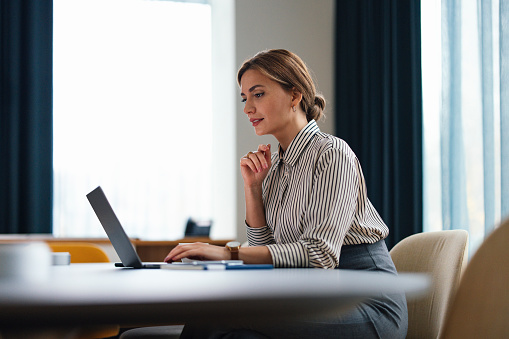 Focused professional woman with a confident look working on a laptop at an office desk, embodying productivity and dedication.