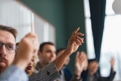 Focused individual raising hand among a group in a meeting.