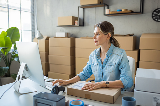 Women, owner of small business packing product in boxes, preparing it for delivery.