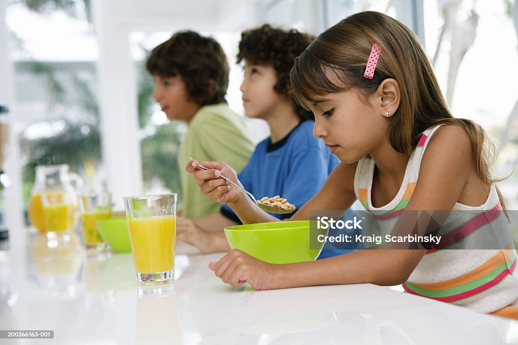 Tres niños (8 a 10) en la mesa, con desayuno - Foto de stock de Cereal de desayuno libre de derechos