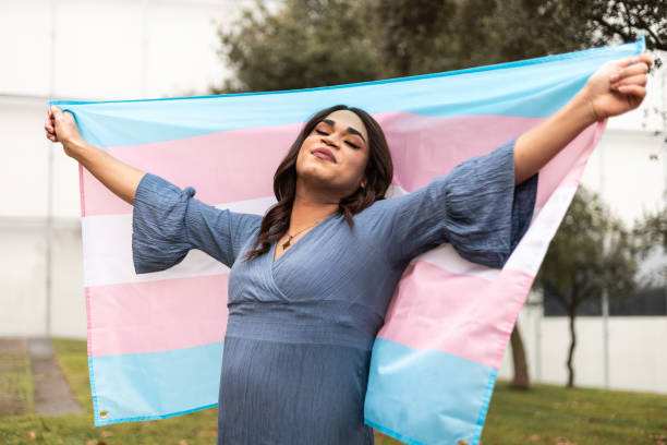 trans woman showing trans flag with proud expression. latin ethnicity. lgtb concept. - transgender pride flagge stock-fotos und bilder