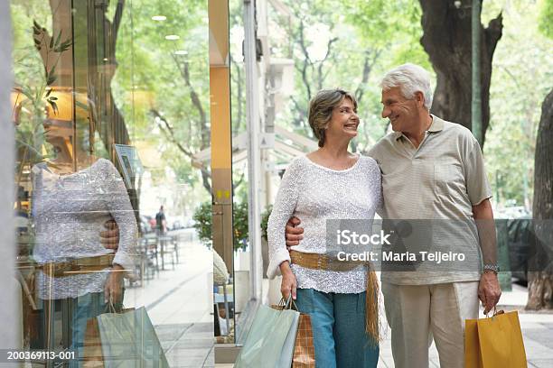 Foto de Casal Sênior Andando Carregando Sacos De Compras Anteriores Sorrindo e mais fotos de stock de Exterior