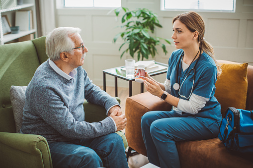 Nurse visiting mature patient at home. She is holding pill bottle and talking to patient how to use it.