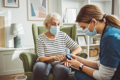 Nurse visiting senior patient at home. She is talking with senior woman about her condition and measuring oxygen in blood.